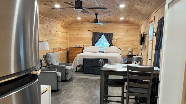Una habitación pequeña y bien iluminada con cama, zona de estar y kitchenette.