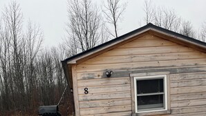 Una pequeña cabaña de madera con el número 8 en el lateral, una ventana y una zona de parrilla cubierta.