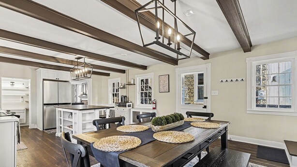 Una cocina moderna con armarios blancos, un refrigerador de acero inoxidable y un comedor con mesa y sillas de madera.