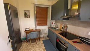 Een kleine keuken met een koelkast, fornuis, spoelbak en een eethoekje met een stoel en tafel.