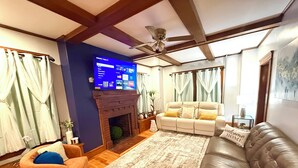 Una sala de estar con chimenea, un sofá, un sillón reclinable, un televisor de pantalla plana y un ventilador de techo.