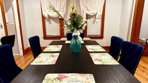 Una mesa de comedor con manteles individuales estampados con motivos florales, sillas tapizadas en azul y un jarrón con flores.
