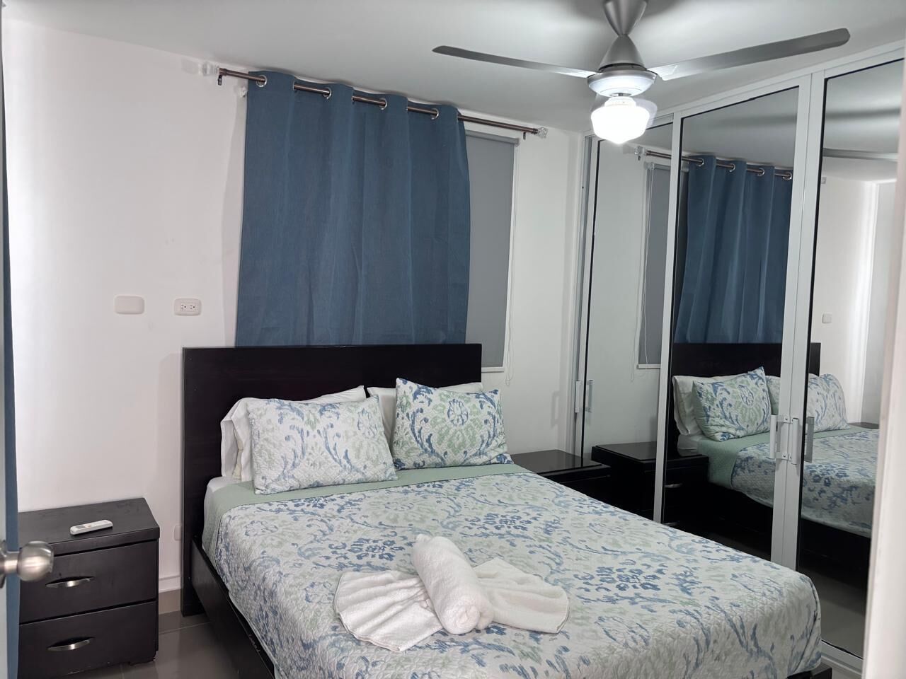 A bedroom with a bed, a nightstand, a mirror, and a ceiling fan.