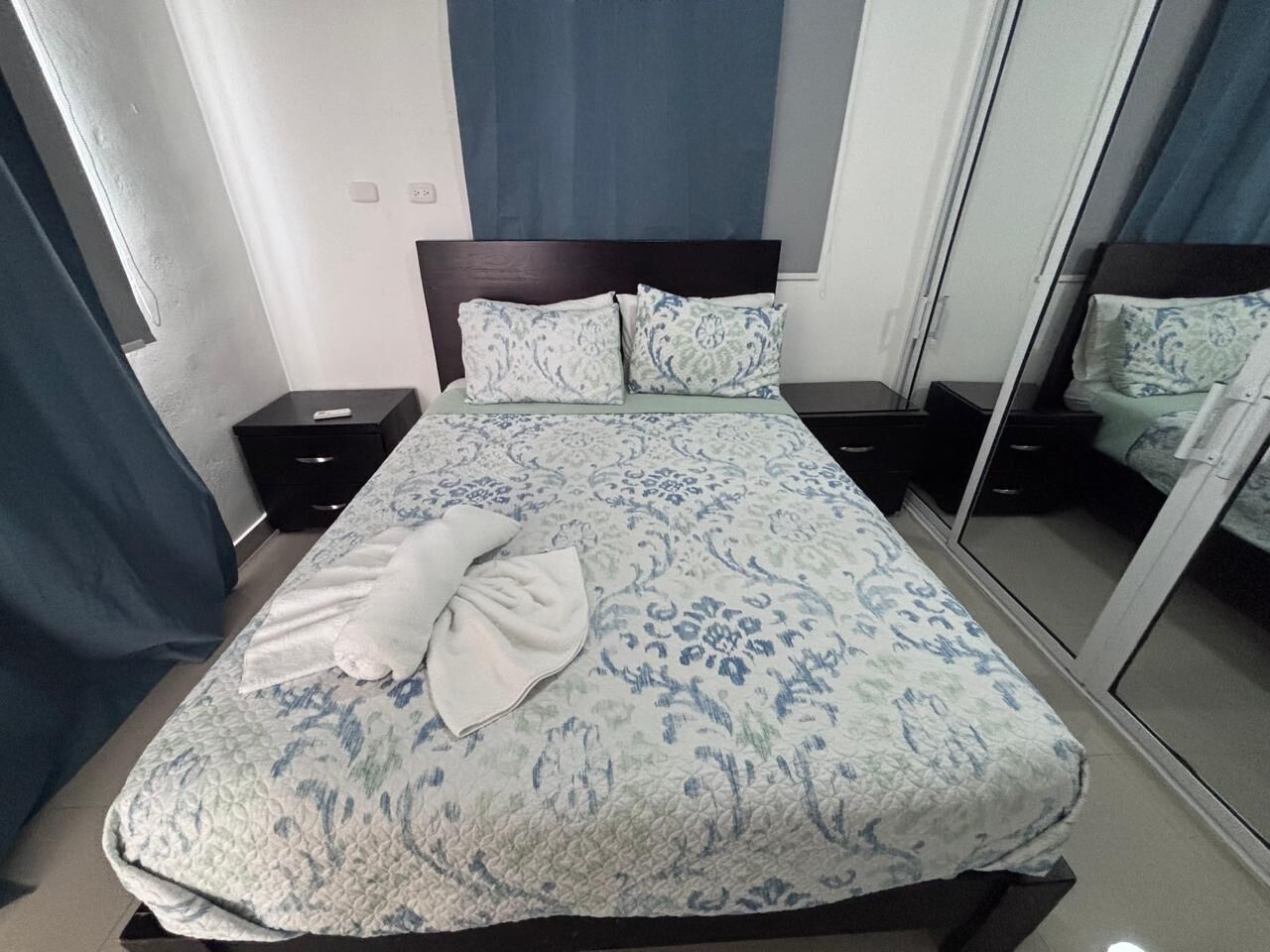 Un letto rifatto con cura, una coperta a motivi decorativi, due comodini e un grande specchio a parete.