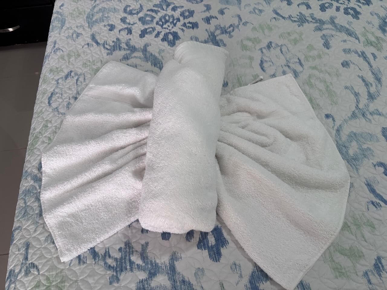 Ein ordentlich gefaltetes weißes Handtuch auf einem Bett mit einem gemusterten Überwurf.