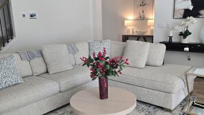 Una sala de estar moderna con un sofá seccional gris, una mesa redonda de centro con un jarrón de flores y una alfombra estampada.