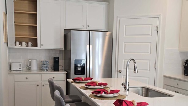 Una cocina moderna con armarios blancos, un refrigerador de acero inoxidable, una cafetera integrada y una zona de asientos con taburetes de bar.