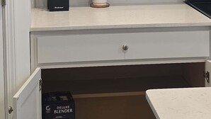 Una cocina con armarios blancos, una encimera, una planta en maceta y una caja de licuadora.