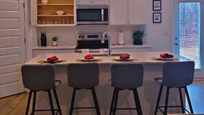 Una cocina moderna con armarios blancos, una isla central con taburetes y una mesa de comedor para cuatro.