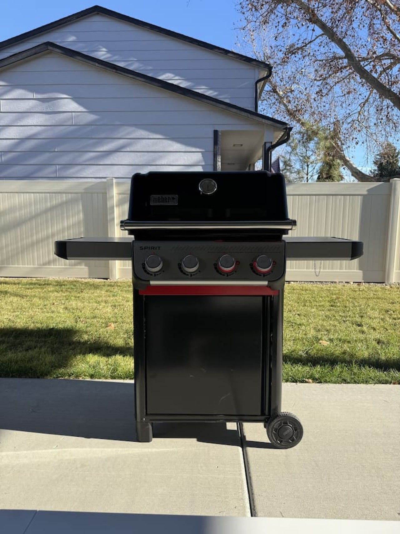 A portable gas grill with a digital display, a side burner, and a small oven, set on a concrete surface.