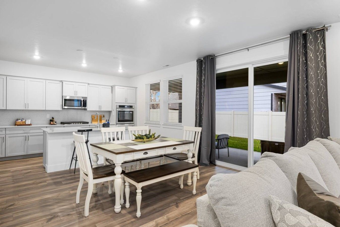A modern kitchen with white cabinets, a dining table with chairs, and a sliding glass door leading to a balcony.