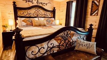Une pièce aux murs lambrissés, avec un lit agrémenté d’une tête de lit décorative et d’un oreiller sur lequel est inscrit le texte : « SOYEZ NOS INVÍTÉS ».