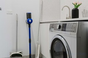 Un área de lavandería con lavadora, un trapeador azul y una escoba.