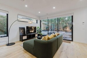 Un salon moderne avec un canapé, un téléviseur et une grande fenêtre donnant sur un jardin.
