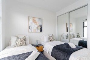 Une chambre moderne avec deux lits, une table de chevet, un miroir et des œuvres d’art accrochées au mur.