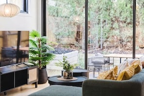 A living room with a TV, a sofa, a coffee table, and a potted plant. - Stylish 4BR Townhouse with Private Courtyard (Box Hill North)