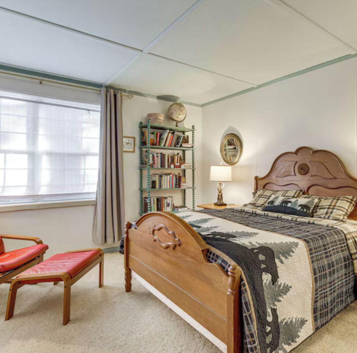 A bedroom with a wooden bed, a red chair, a bookshelf, and a window with curtains.