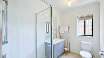 A bathroom with a glass shower enclosure, a sink, a toilet, and a window with a view.