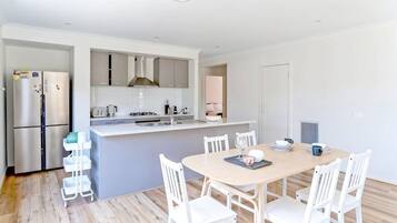 A modern kitchen with white cabinets, a central island, and a dining area with white chairs.
