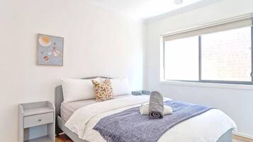 Un dormitorio con cama, mesita de noche, ventana y una obra de arte en la pared.