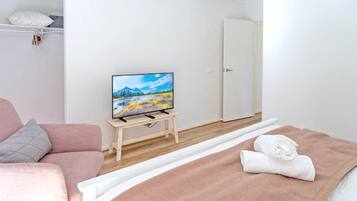 A bedroom with a bed, a television on a stand, a pink sofa, and a white door.