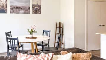 A dining area with a round table, chairs, and a potted plant. There is a coat rack and a door in the background.