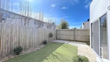Un patio trasero con cerca de madera, césped y zona de patio empedrada.