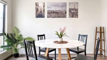 Un comedor con una mesa redonda, cuatro sillas, una planta en maceta y tres cuadros en la pared.