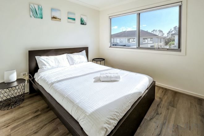 A neatly made bed with white linens, a bedside table with a lamp, and a window with a view of buildings.