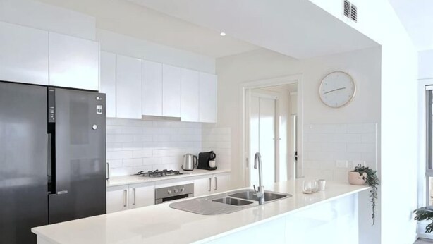 Una cocina moderna con armarios blancos, un refrigerador de acero inoxidable, una estufa a gas y un lavamanos.