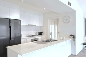 A modern kitchen with white cabinetry, a stainless steel refrigerator, a gas stove, and a sink. - Stylish Berwick Home with WiFi, Smart TV, Garage (Berwick)