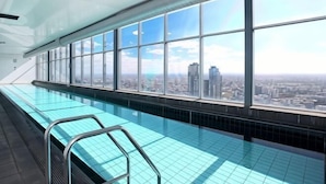 Une piscine intérieure moderne avec vue sur la ville, de grandes fenêtres et un ciel dégagé.