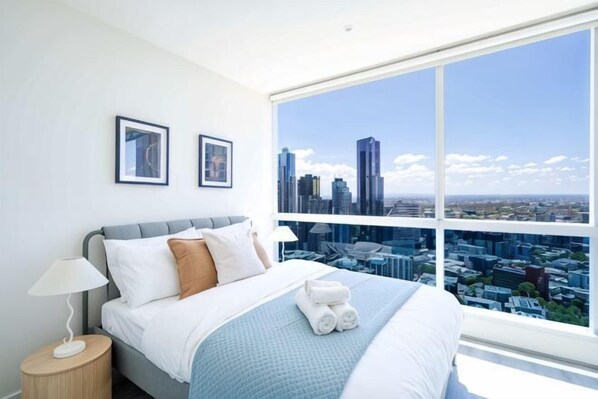 A hotel room with a large bed, a nightstand, a lamp, and a city view. - lvl42 2B APT with Free Parking in CBD (Melbourne)