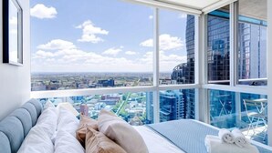Une chambre avec une grande fenêtre, un lit avec des oreillers et une vue sur le paysage urbain.