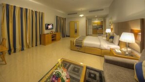 A hotel room with a bed, a sofa, a TV, a desk, and a bathroom visible in the background. - City Stay Grand Hotel Apartments - Al Barsha (Dubai)