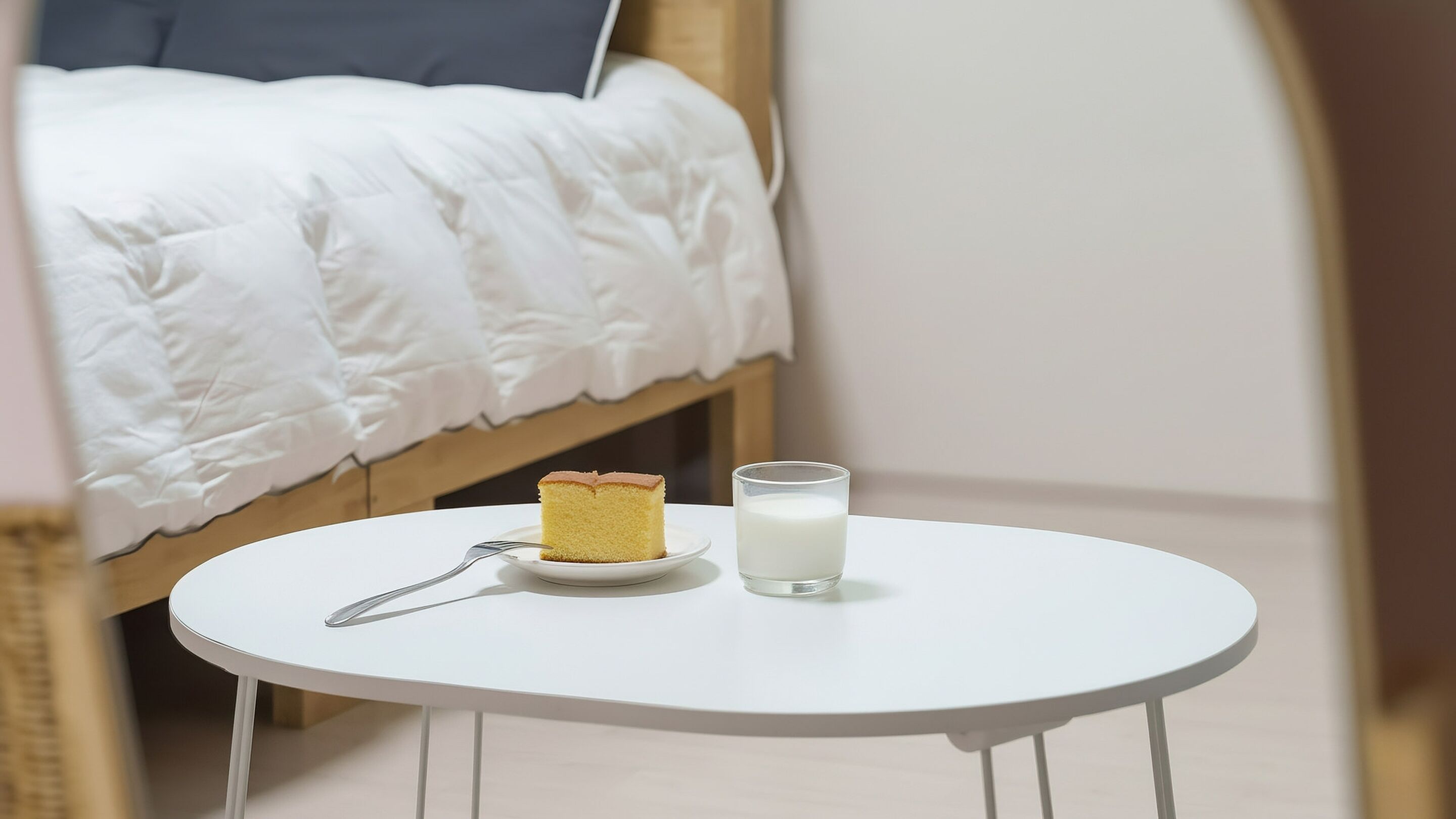 Una pequeña mesa redonda con una porción de pastel y un vaso de leche.