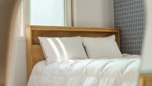 Una cama con cabecera de madera, ropa de cama blanca y una pared estampada al fondo.