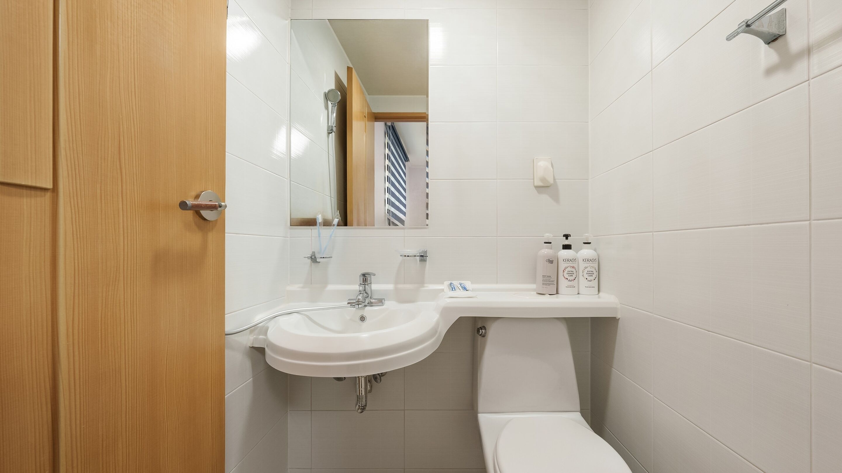 Un baño con lavamanos blanco, espejo e inodoro. Hay artículos de aseo en la encimera del lavamanos.