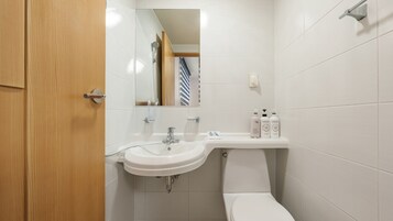 Un baño con lavamanos blanco, espejo e inodoro. Hay artículos de aseo en la encimera del lavamanos.