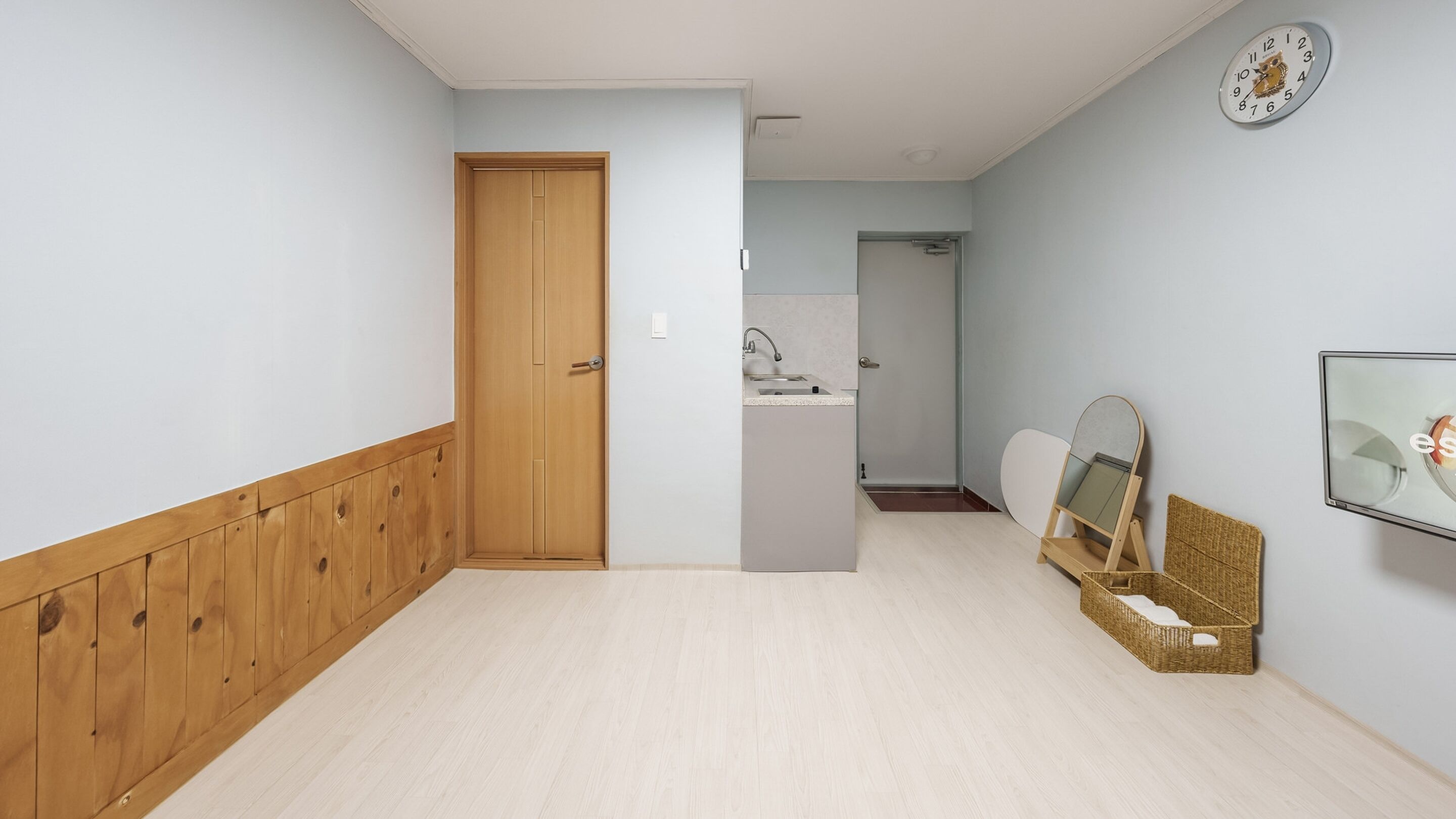 Un corridoio con una porta in legno, un lavandino e uno specchio appeso al muro.