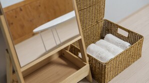 A wicker basket with towels inside, placed on a wooden floor next to a wooden cabinet with a white shelf. - Boryeong Jeil Pension (Boryeong)