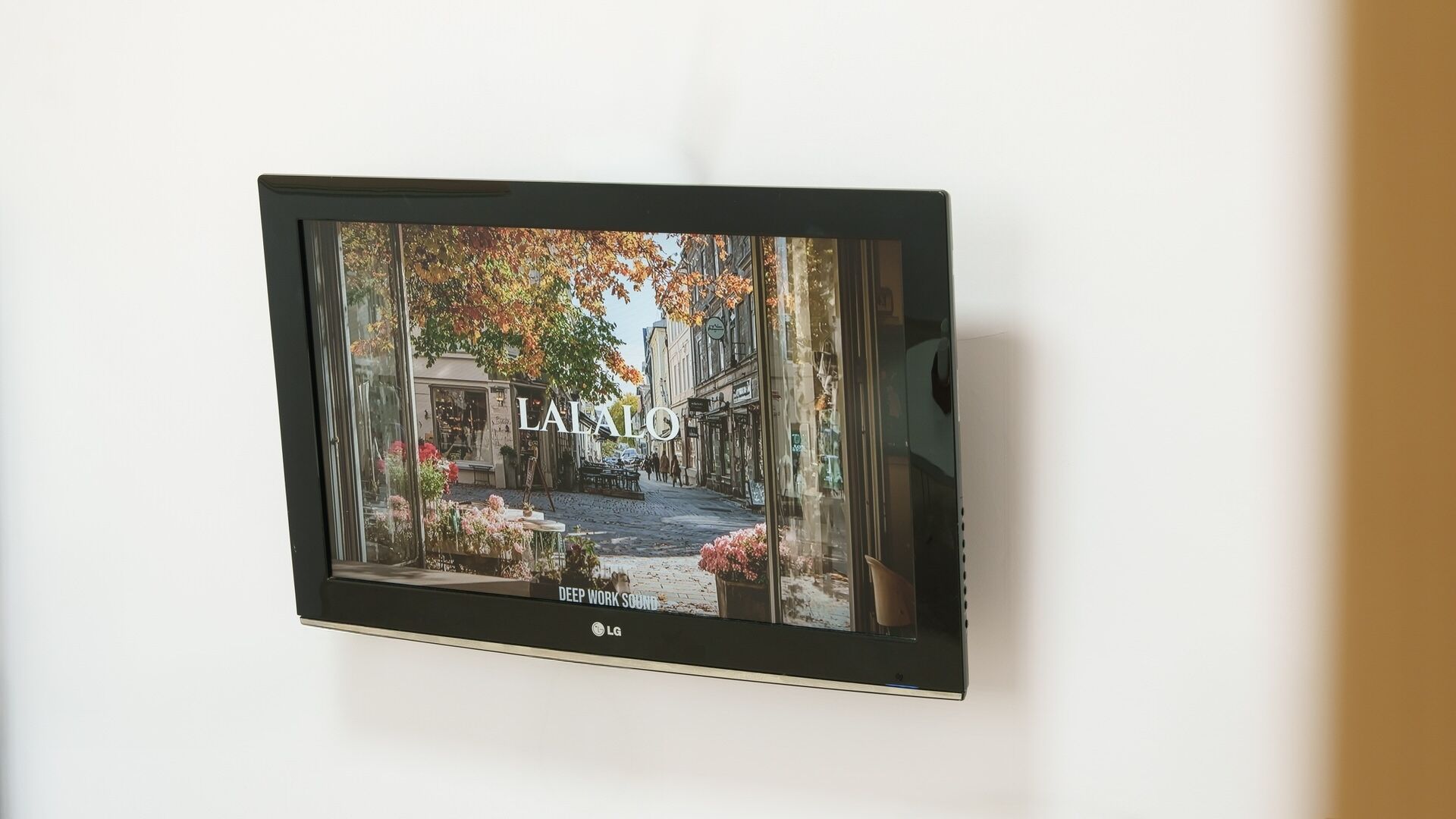 Televisor de pantalla plana montado en una pared que muestra una escena de calle con una fachada que dice 'LA SALO'.