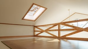 Una habitación con techo inclinado, vigas de madera y tragaluces.