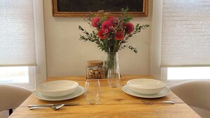 Une table à manger avec deux assiettes blanches, deux verres vides et un vase contenant des fleurs roses.