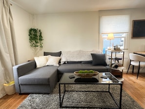 A modern living room with a grey sectional sofa, a glass coffee table, and a small side table with a lamp.