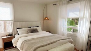 Une chambre à coucher avec un grand lit, une table de chevet, une lampe suspendue et une fenêtre avec des rideaux.