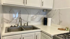 Cocina con gabinetes blancos, un lavamanos doble, estufa y salpicadero de mármol.