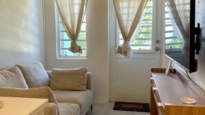 Un espacio habitable pequeño con sofá, televisor sobre un pie de madera y una puerta con cortinas.