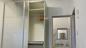 Un dormitorio con cama, vestidor, baño con espejo y ventilador de techo.