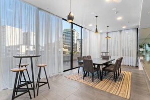 A modern dining area with a table and chairs, large windows with sheer curtains, and city views. - Luxe 2BR Retreat POOL, GYM & PARKING South Yarra (South Yarra)